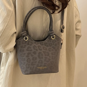 Chic leopard print bucket bag with gold lettering and woven handles shown on a model