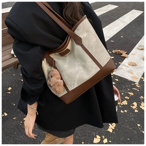Canvas tote bag with leather trim and brown teddy bear charm in a street scene