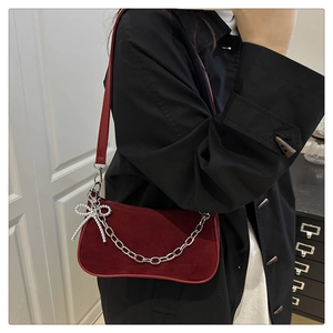 Detail of dark red suede baguette bag featuring silver chain and bow pendant decoration