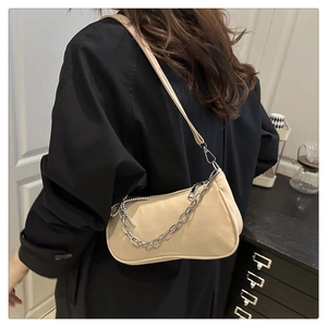 Detail of beige hobo bag with silver chain and pearl beads worn over a black blazer