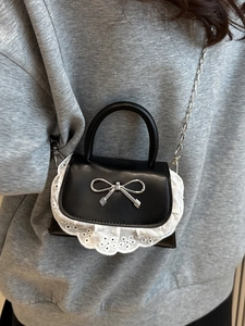Elegante mini borsa nera con fiocco argento e bordo in pizzo bianco su sfondo grigio
