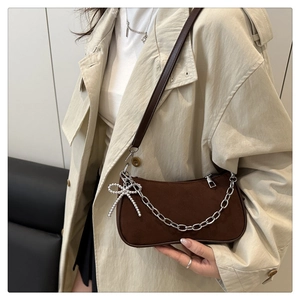 Detail of brown suede crescent bag featuring silver chain and pearl bow charm on trench coat
