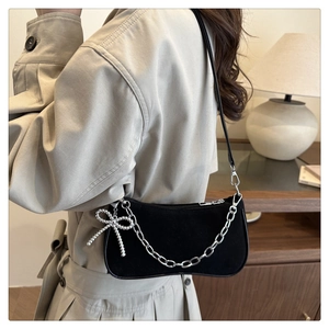 Detail of black suede hobo bag with silver chain strap and pearl bow charm accessory