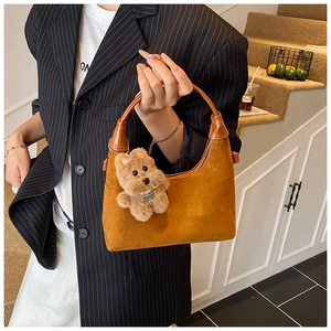 Close-up of brown suede hobo bag with plush puppy charm and leather handle detail