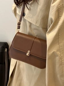 Classic brown leather baguette bag with gold metal buckle on a beige trench coat
