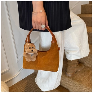 Detail of brown suede tote bag featuring a cute plush bear charm and leather handle