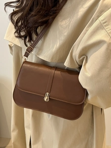 Retro dark brown leather baguette bag with gold buckle on a beige trench coat model