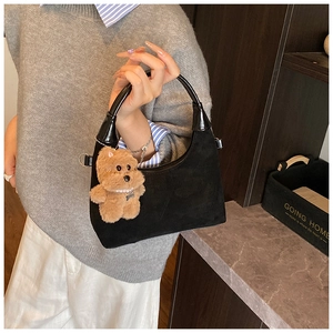 Detail of black suede hobo bag with polished leather handle and cute teddy bear charm