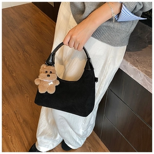 Detail of black suede hobo bag with glossy leather handle and plush bear charm
