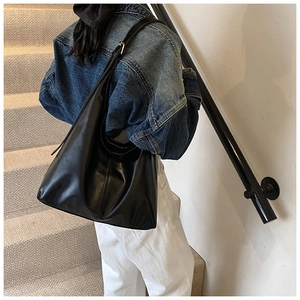 Close-up of minimalist black PU leather tote bag with adjustable strap and gold buckle