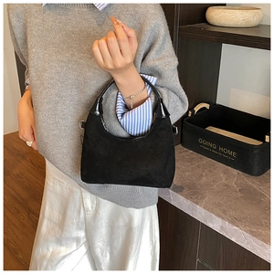 Detail of black crescent handbag in suede material with glossy leather handle on a model