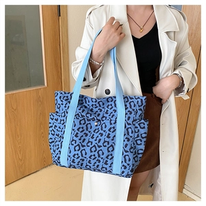Detail of large leopard print tote bag with blue straps shown on a shoulder