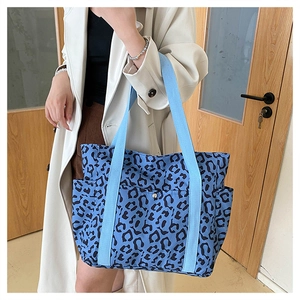 Detailed close-up of a blue leopard print tote bag with woven straps and front pocket