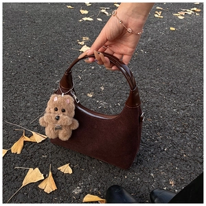 Close-up of brown suede saddle tote bag with a cute plush dog charm on autumn leaves