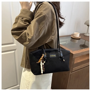Detail of black suede tote bag with FASHION label and colorful wooden bead charm