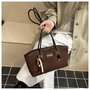 Detail of dark brown suede tote bag featuring fashion tag and beaded tassel accessory