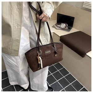 Close-up of deep brown suede tote with a decorative beaded tassel and fashion label