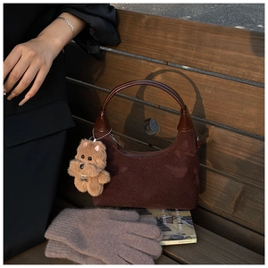 Detail of dark brown suede hobo bag with leather handle and cute puppy charm on wooden bench