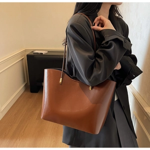 Brown leather tote bag featuring golden metal buckles and long shoulder straps on a model