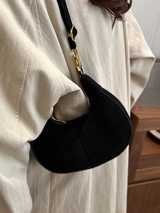 Minimalist black matte hobo bag with gold hardware worn by a model in a neutral setting