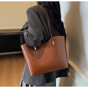 Dark brown leather tote bag with curved top edge detail and golden metal accents