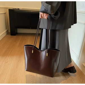 Detail of dark brown leather tote bag with gold metal hardware and long shoulder straps