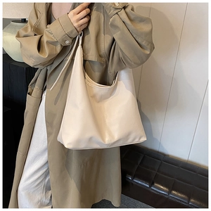 Detailed side view of large off-white leather tote bag styled with a khaki trench coat