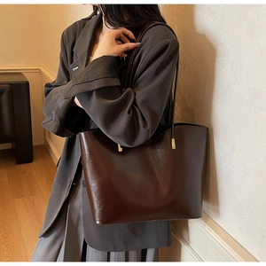 Detail of glossy dark brown tote bag with thin shoulder straps and gold hardware