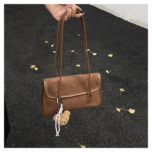 Close-up of brown matte suede underarm bag with smooth leather trim and bear charm