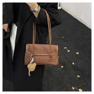 Detail of dark brown suede shoulder bag with cute bear charm worn on black coat