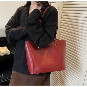 Detail of dark red glossy leather tote bag with gold hardware held by a model