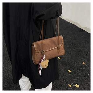 Detail of a brown suede shoulder bag featuring a plush bear charm and ribbon accent