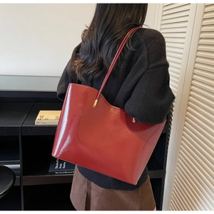 Model carrying a large burgundy tote bag with a glossy oil-wax finish and long handles