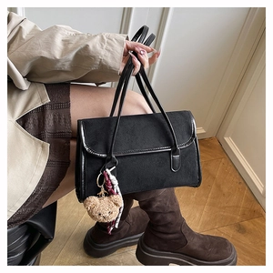 Detail of black matte suede shoulder bag with plush bear charm and silk scarf