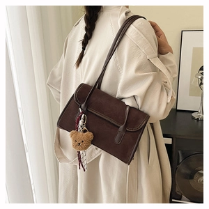Detail of dark brown suede shoulder bag featuring a cute plush bear and striped ribbon charm