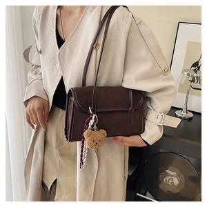 Detail of dark brown suede shoulder bag with cute plush bear charm and sleek strap