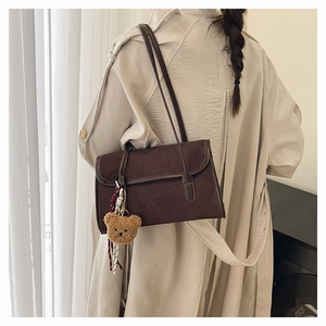 Detail of dark brown matte leather shoulder bag with cute plush bear charm on white coat
