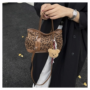 Detail view of leopard print bucket bag with brown leather trim and plush bear charm