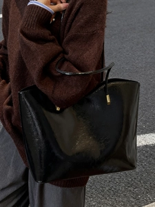 Glossy black leather tote bag with gold hardware worn by a model in a street style view
