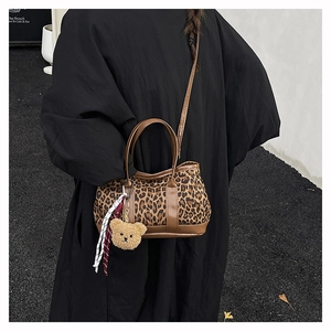 Detail of leopard print bucket bag with brown leather handles and plush bear charm