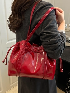 Glossy red PU leather tote bag with bow detail and drawstring shown on shoulder