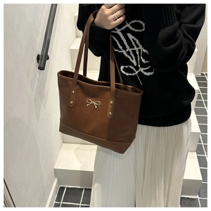 Close-up of brown faux leather tote bag with gold bow clasp and rivets on female model
