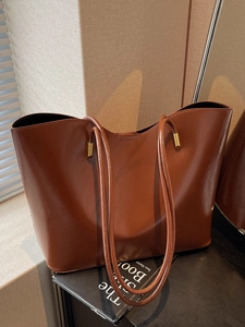 Brown faux leather tote bag with glossy finish and slim straps on a minimalist setting