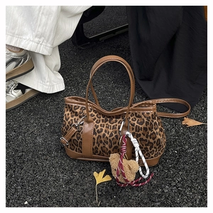 Detail of leopard print crossbody bag with plush bear charm and brown leather trim on pavement