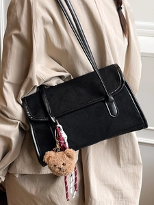 Minimalist black matte shoulder bag with plush bear charm and contrast braided rope detail