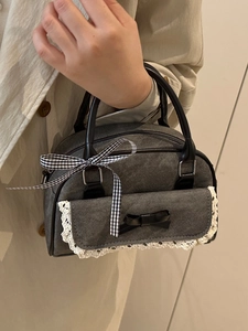 Gray denim bow handbag with lace trim and black leather handles shown by model