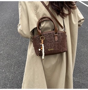 Detail of dark brown leopard print crossbody bag with beaded charm on khaki trench coat