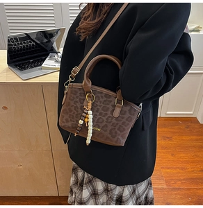 Detail of leopard print handbag with golden brand logo and ethnic bead pendant decoration