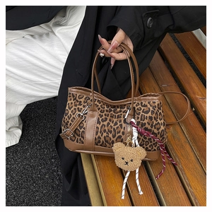 Detail of leopard print bucket bag featuring brown faux leather trim and plush bear charm