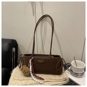 Close-up of brown suede baguette bag featuring side drawstrings and a plush bear charm